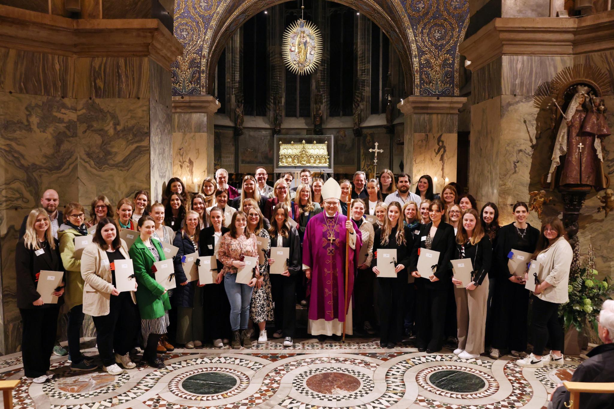 Menschen mit Urkunden in der Hand  stehen um Bischof Dieser im Aachener Dom vor dem Altar