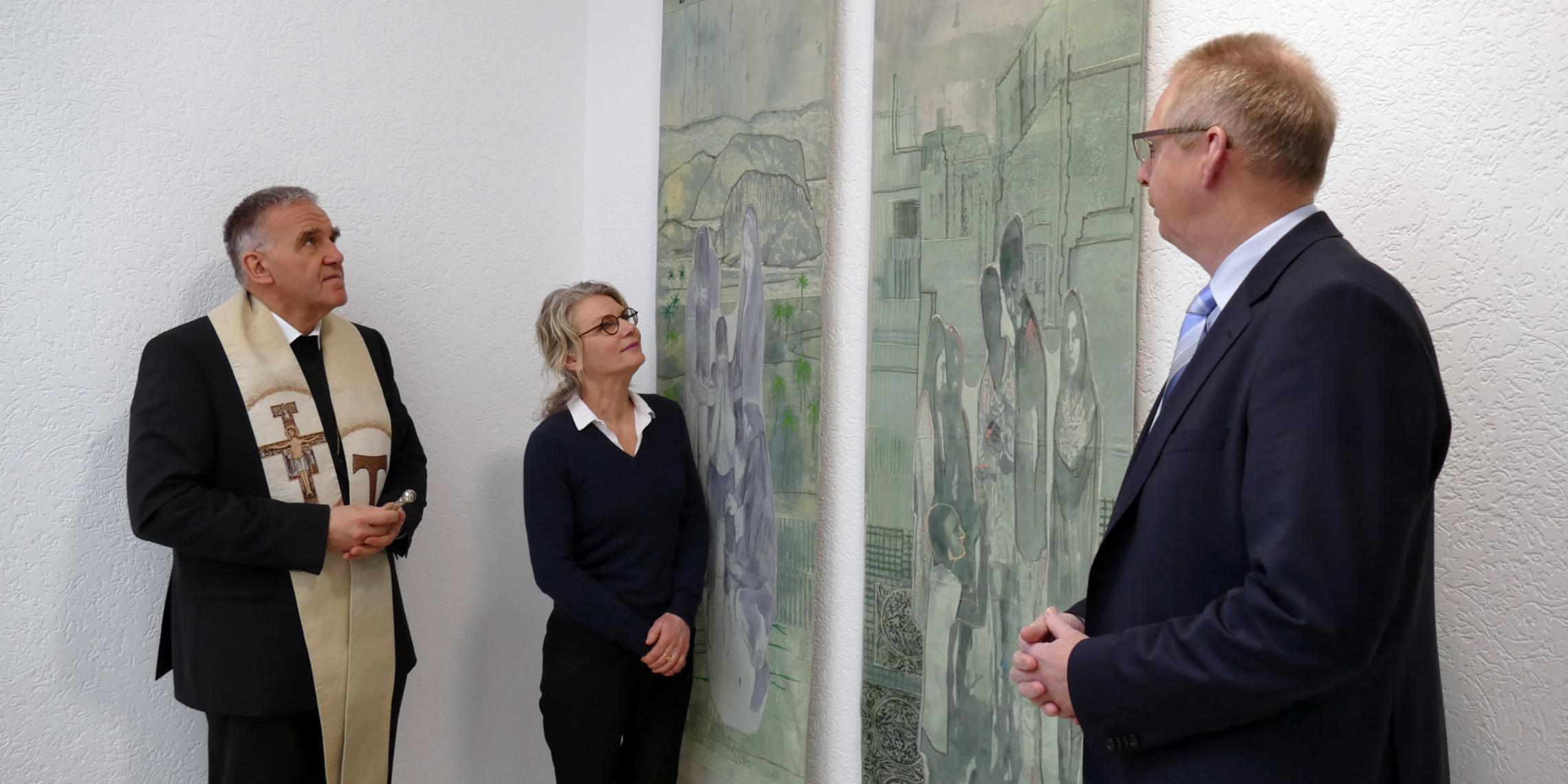 Der Vorsitzende des Caritasverbandes für das Bistum Aachen, Weihbischof Dr. Johannes Bündgens (.), und die Künstlerin Vera Sous  erläuterten die Banner und ihren Entstehungsprozess. Diözesancaritasdirektor Burkard Schröders (r.) freut sich, dass die Kunstwerke nun im Haus der Caritas hängen.