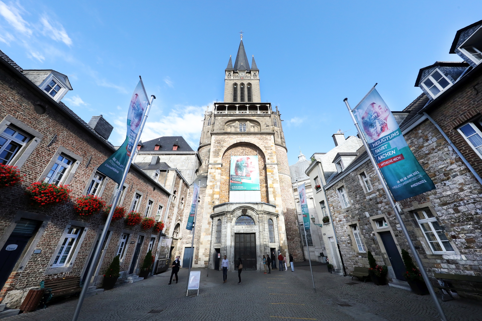 Rund um den Aachener Dom erstrahlt nicht nur auf zahlreichen Fahnen das Grün der Heiligtumsfahrt: Über dem Hauptportal des Doms weist ein Großtransparent auf die Wallfahrt hin, die vom 18. bis 28. Juni 2021 stattfindet. (c) Domkapitel Aachen / Andreas Steindl