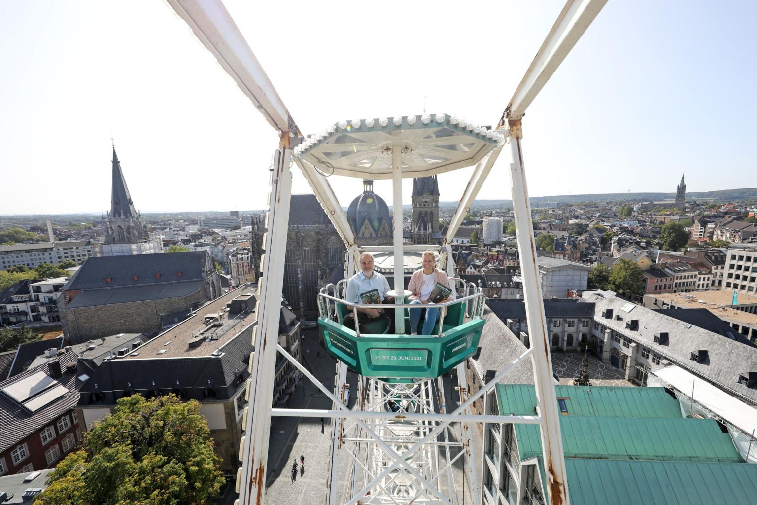 Mit der grünen Gondel zur Heiligtumfahrt Aachen geht es hoch hinaus: Am höchsten Punkt erreicht das Riesenrad 45 Meter Höhe und bietet einen großartigen Blick auf den Aachener Dom. Das ließen sich auch Dompropst und Wallfahrtsleiter Rolf-Peter Cremer sowie Projektmitarbeiterin Nadine Braun nicht entgehen. (c) Domkapitel Aachen / Andreas Steindl