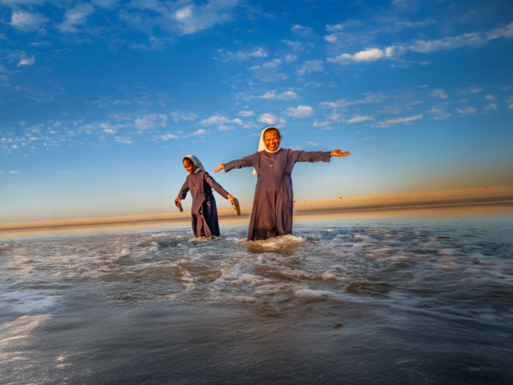 Frau steht im Wasser unter blauem Himmel, lchelt freundlich und streckt die Arme aus