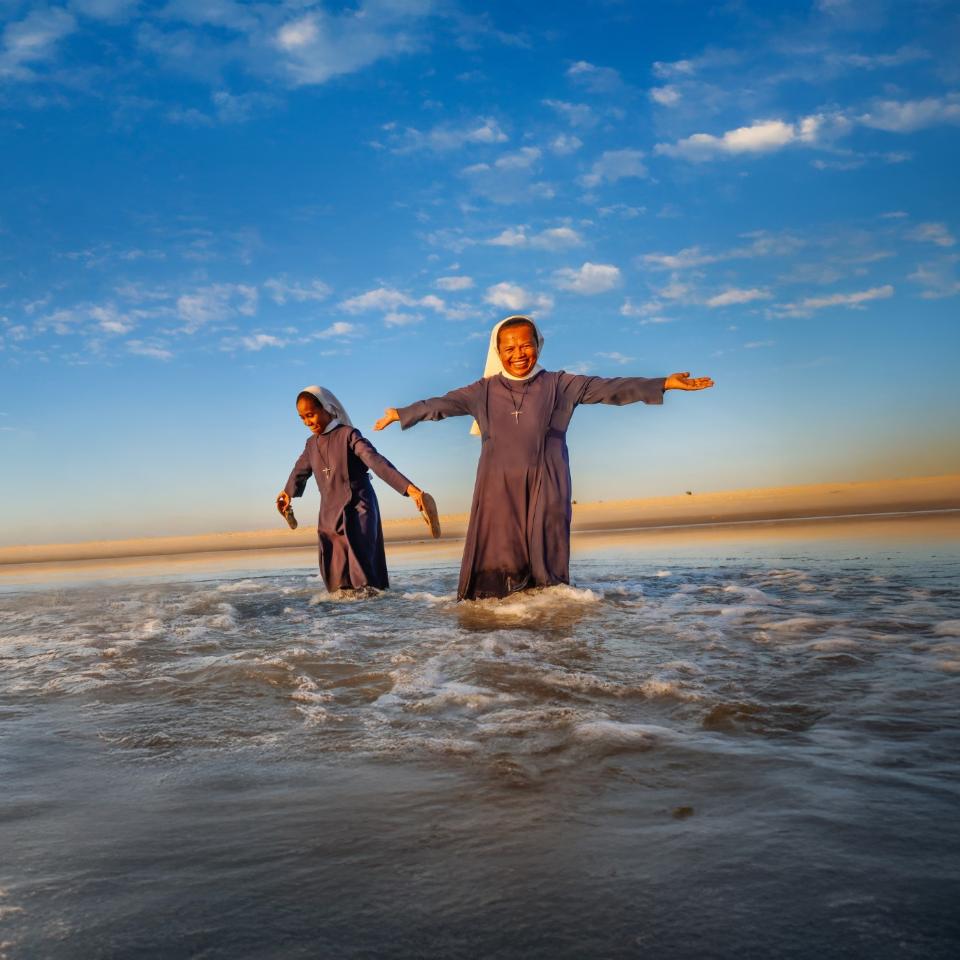Frau steht im Wasser unter blauem Himmel, lchelt freundlich und streckt die Arme aus