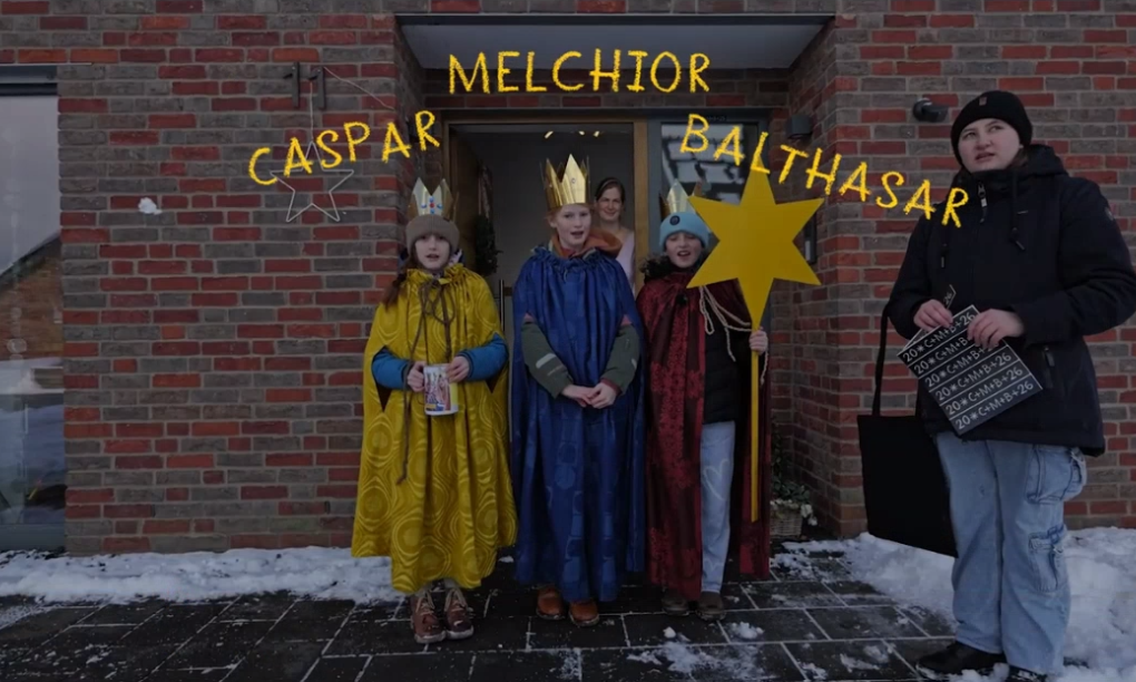 Sternsinger stehen vor einem Haus, mit Gewändern, darüber die Namen Caspar, Melchior Balthasar