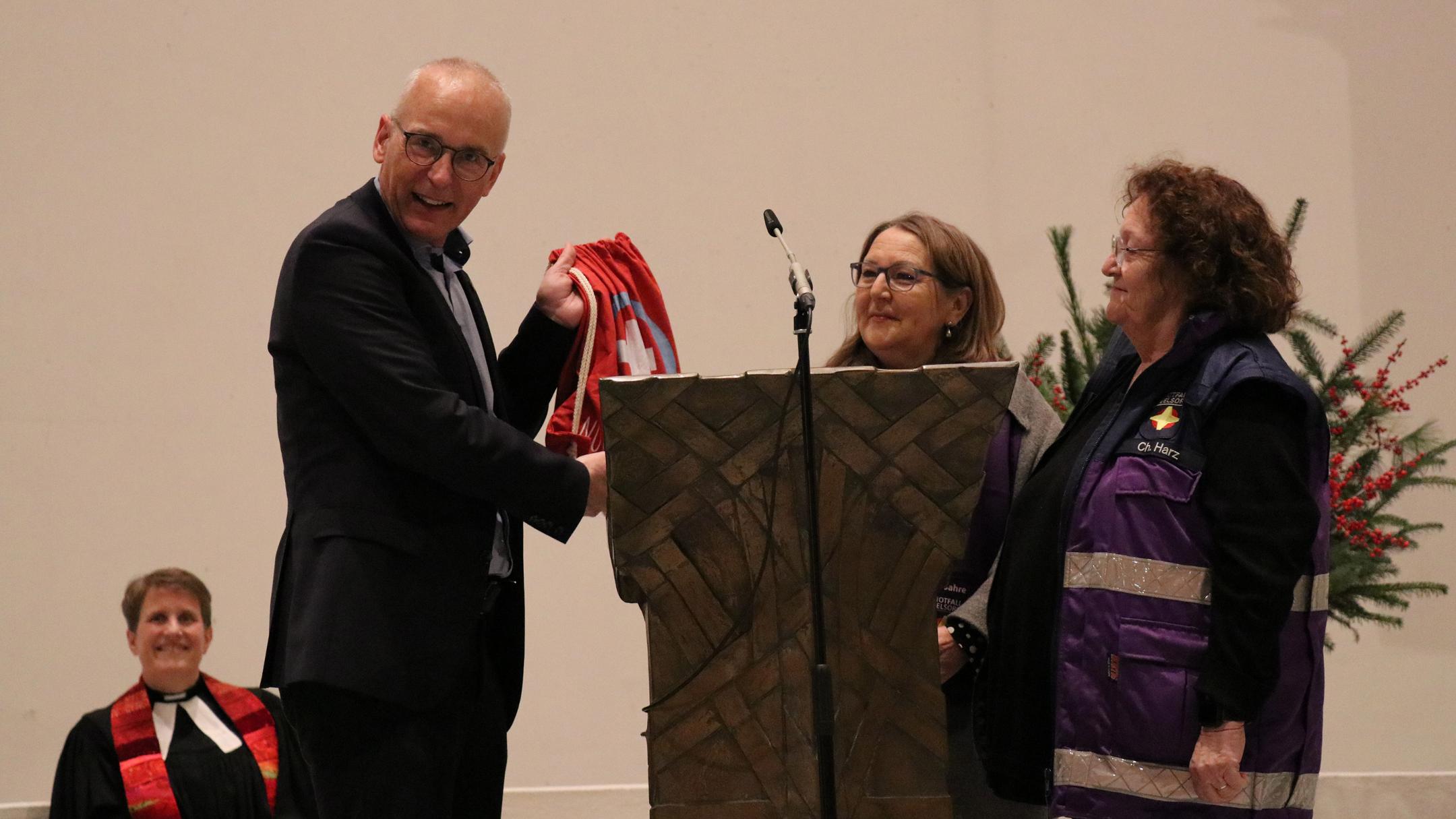 Andreas Dovern, Leiter Brandschutz, Rettungsdienst und Bevölkerungsschutz bei der Städteregion Aachen, würdigte die Arbeit der Notfallseelsorge und betonte, dass diese Verlässlichkeit, Sicherheit und Rückhalt in schwierigen Situationen gebe. Patrick Philipp, Referent für Notfallseelsorge im Bischöflichen Generalvikariat, sprach Grüße im Namen des Bistums Aachen aus. (Foto: C. Braun) Patrick Philipp, Referent für Notfallseelsorge im Bischöflichen Generalvikariat, sprach Grüße im Namen des Bistums Aachen aus. Die Ehrenamtlichen Therese Mauer und Charlotte Harz überreichten Thilo Esser den praktischen und lustigen Notfall-Beutel. (Foto: C. Braun) Die Ehrenamtlichen Therese Mauer (Mitte) und Charlotte Harz überreichten Thilo Esser den praktischen und lustigen Notfall-Beutel.