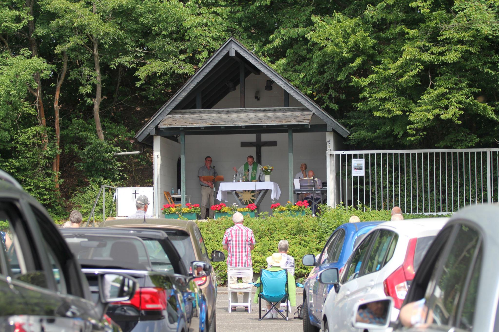 Geparkte PKW und menschen bei einem Gottesdienst unter freiem Himmel.