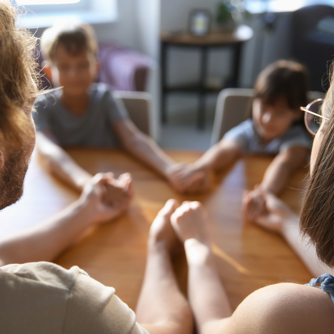 Familie sitzt am Tisch und reicht sich die Hände
