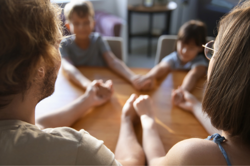 Familie sitzt am Tisch und betet