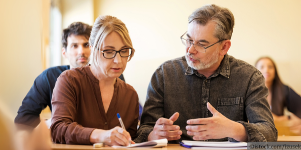 Erwachsene Lernende sitzen und diskutieren an einem Schreibtisch