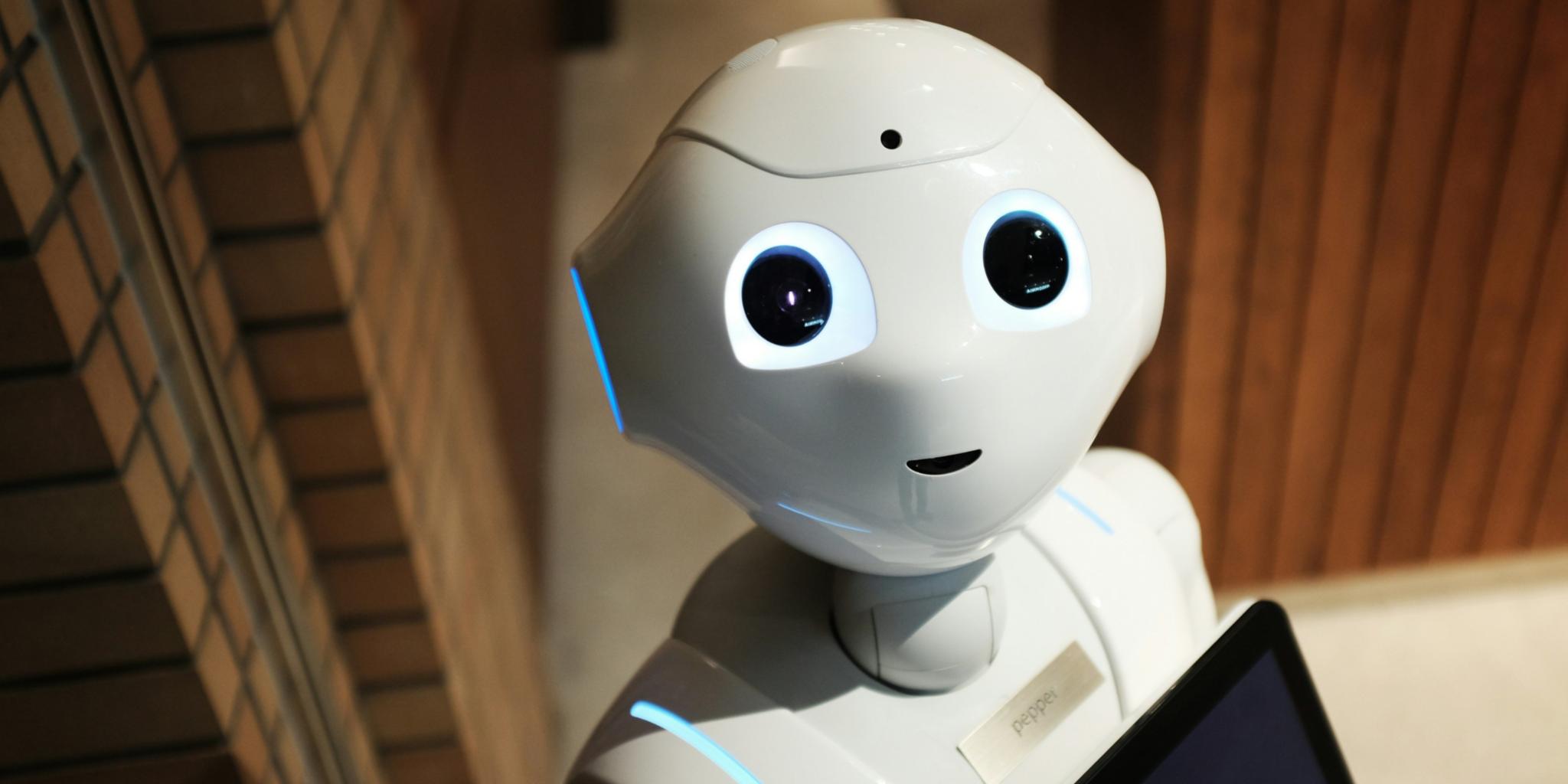 Roboter mit menschlichem Gesicht und einem Tablet in der Hand schaut in die Kamera