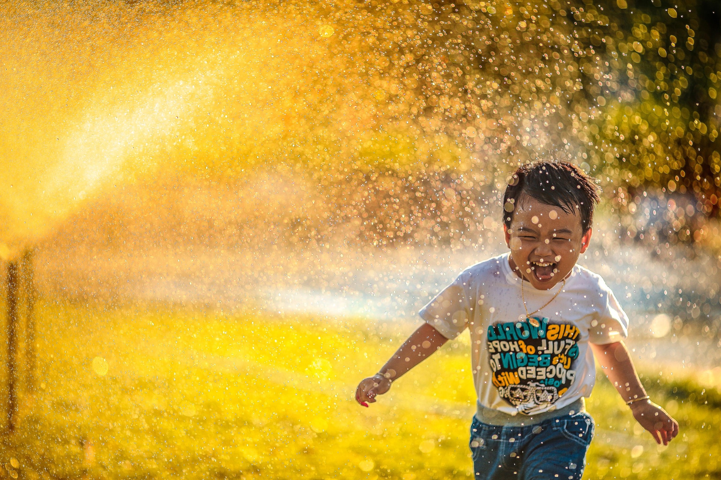 Kleiner Junge läuft im Sonnenschein lachend durch einen Wassersprinkler