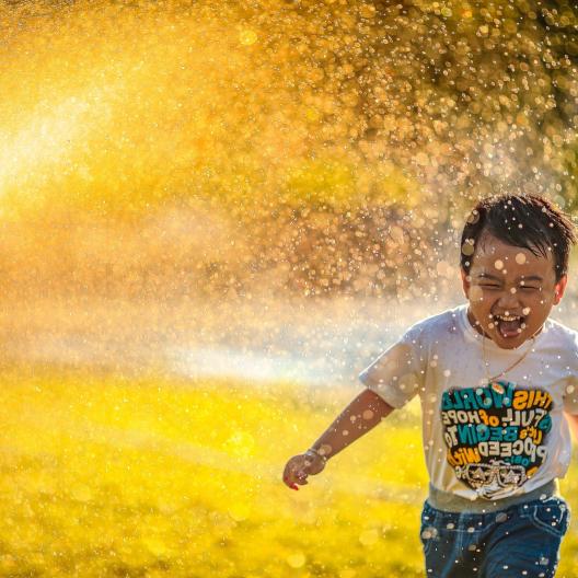 Kleiner Junge läuft im Sonnenschein lachend durch einen Wassersprinkler