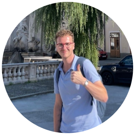 Junger Mann, Mitte 20, Brille, blonde Locken, in mediterraner Umgebung, Daumen hoch, lächelnd