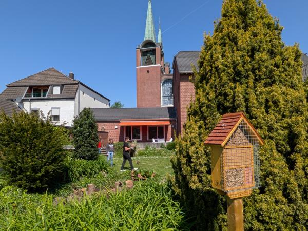 Das Bild zeigt einen Garten mit viel Wiese und einem Vogelhaus. Im Hintergrund sind ein Haus und eine Kirche
