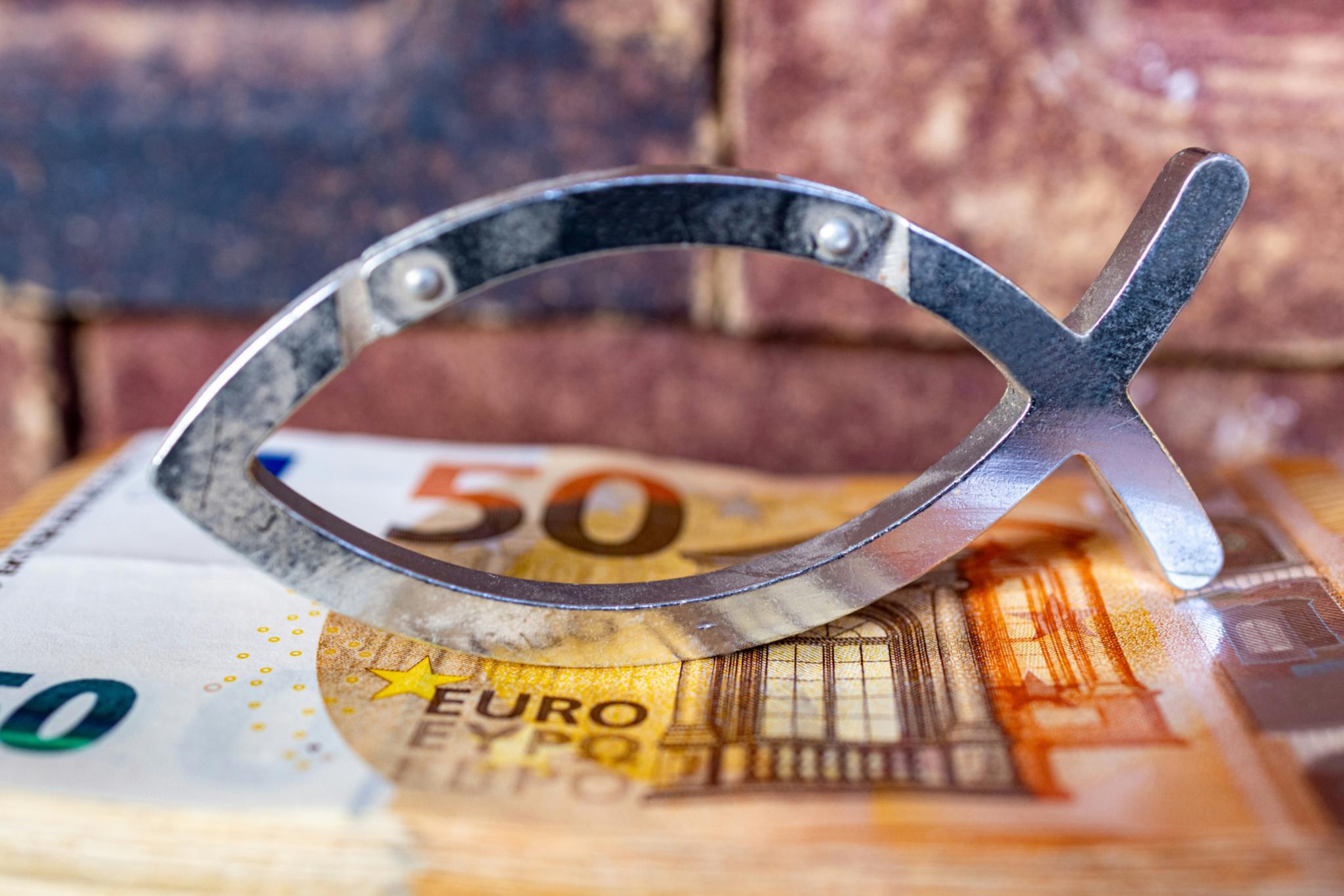 Das christliche Symbol eines Fisches ist aus Metall in zwei schlichten Linien gebildet. Es steht auf einem 50-Euro-Schein.