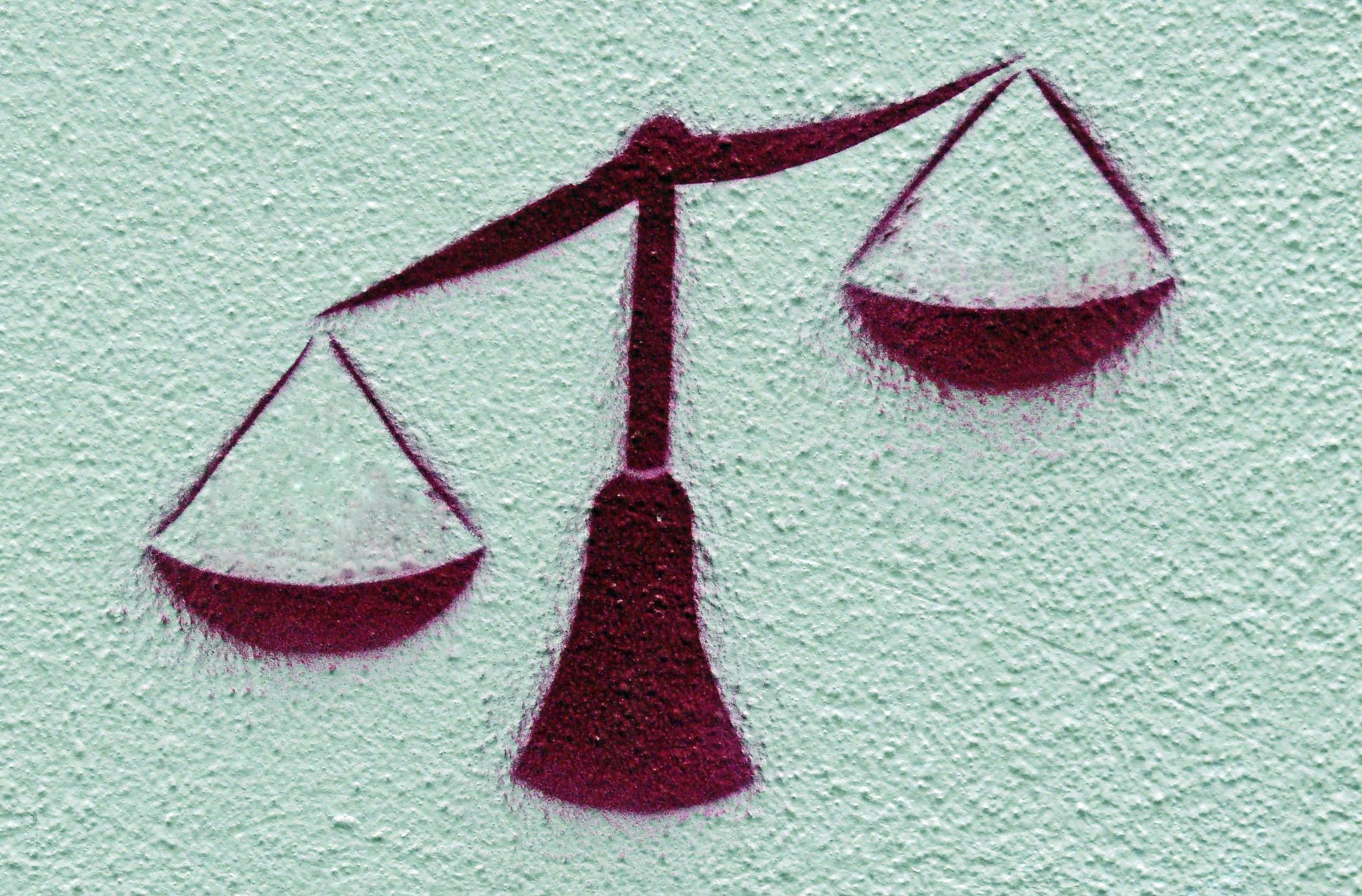 Graffito: An die Wand gesprayte Waage, die linke Waagschale ist tief, die rechte hoch.