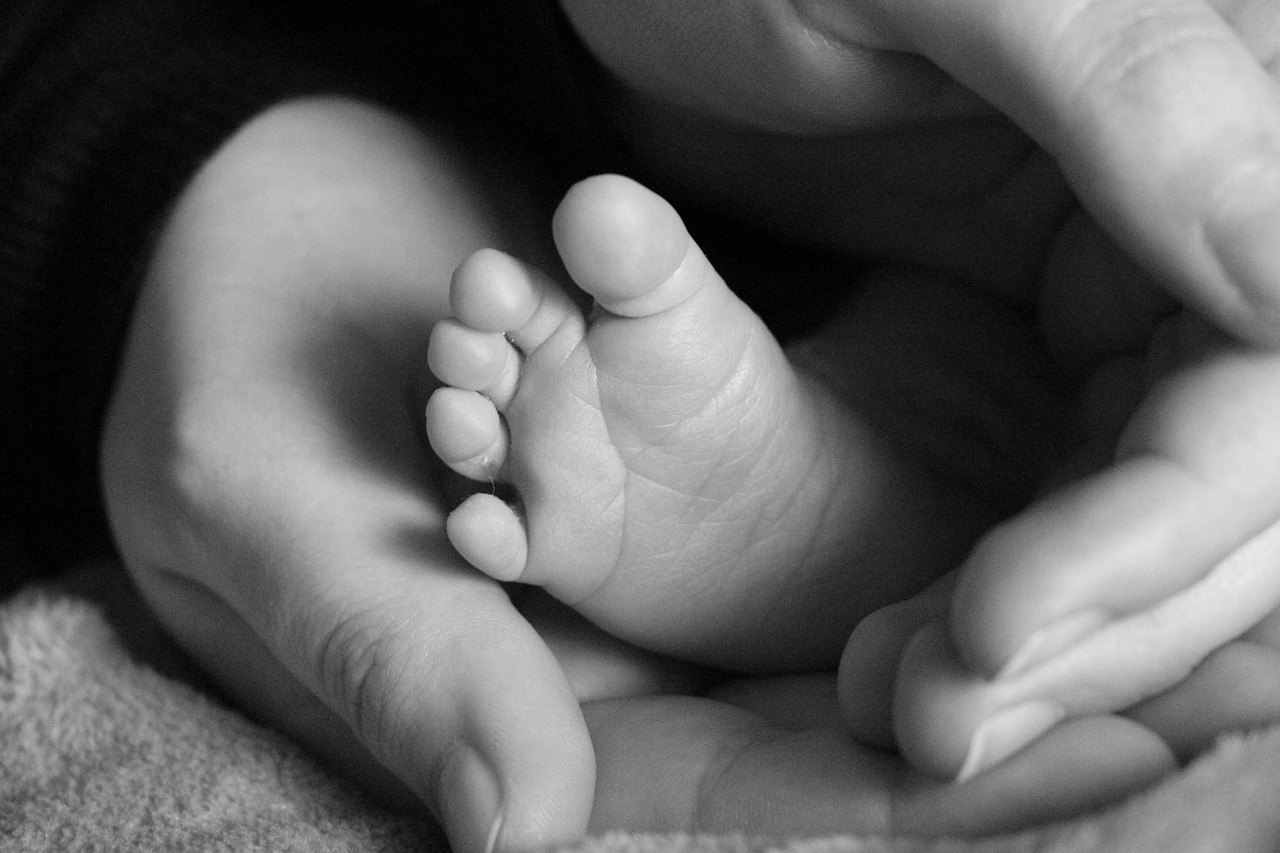 Erwachsenenhände umschließen einen Babyfuß.