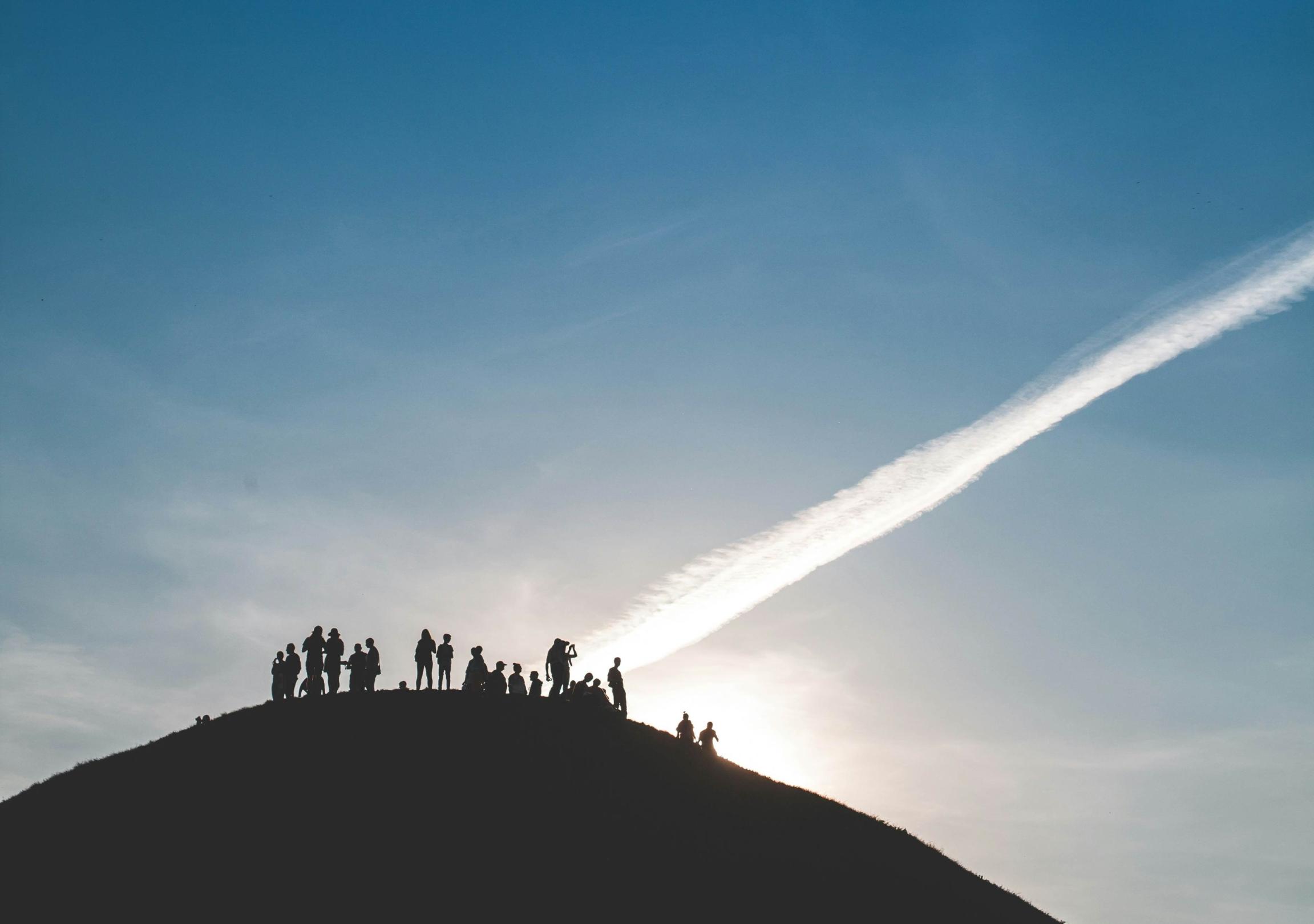 Eine Gruppe von Menschen steht auf einem Hügel und schaut in den Himmel.