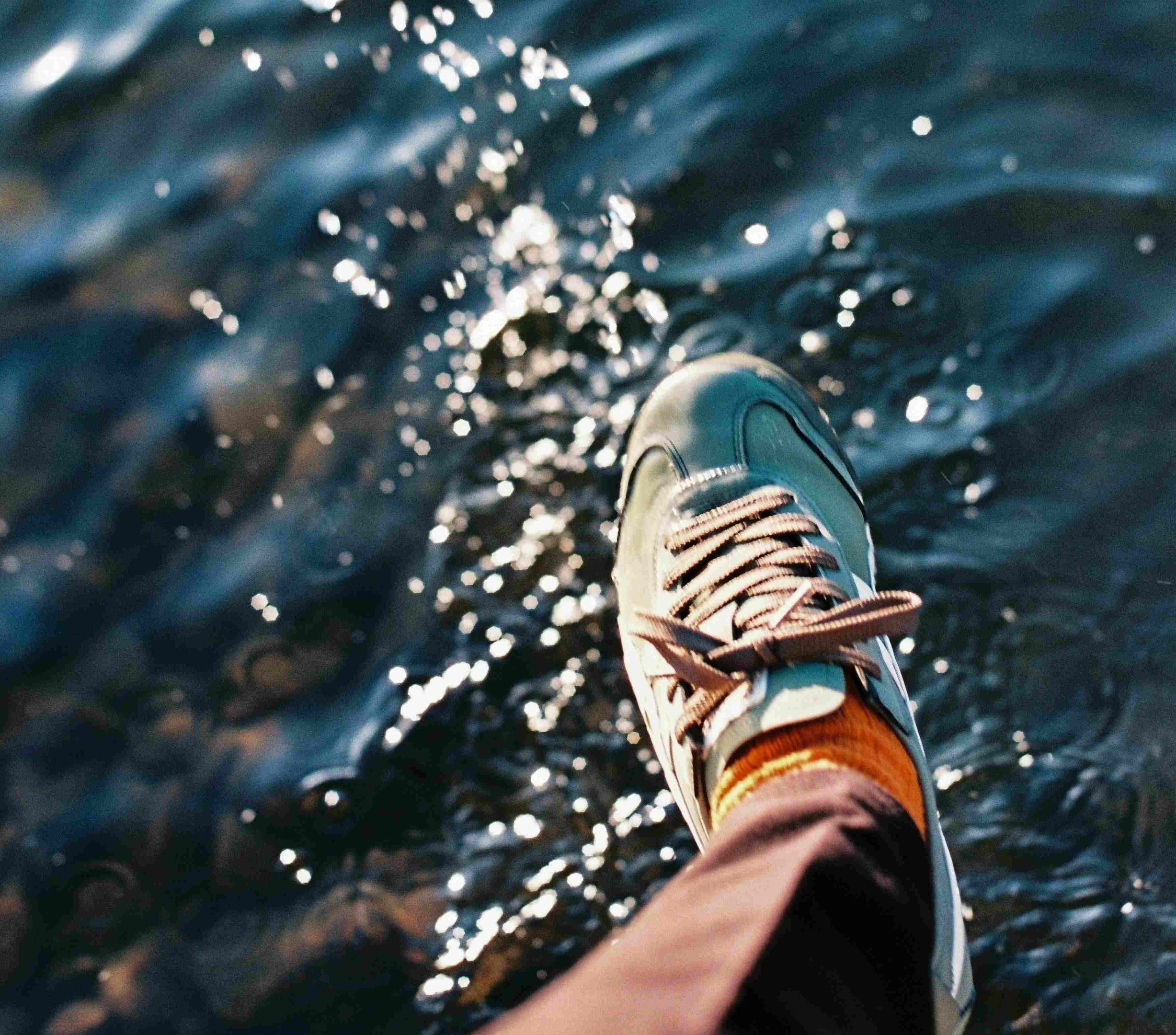 Ein Fuß mit einem Turnschuh schwebt über einer glitzernden Wasseroberfläche, als wolle er gleich darauftreten.