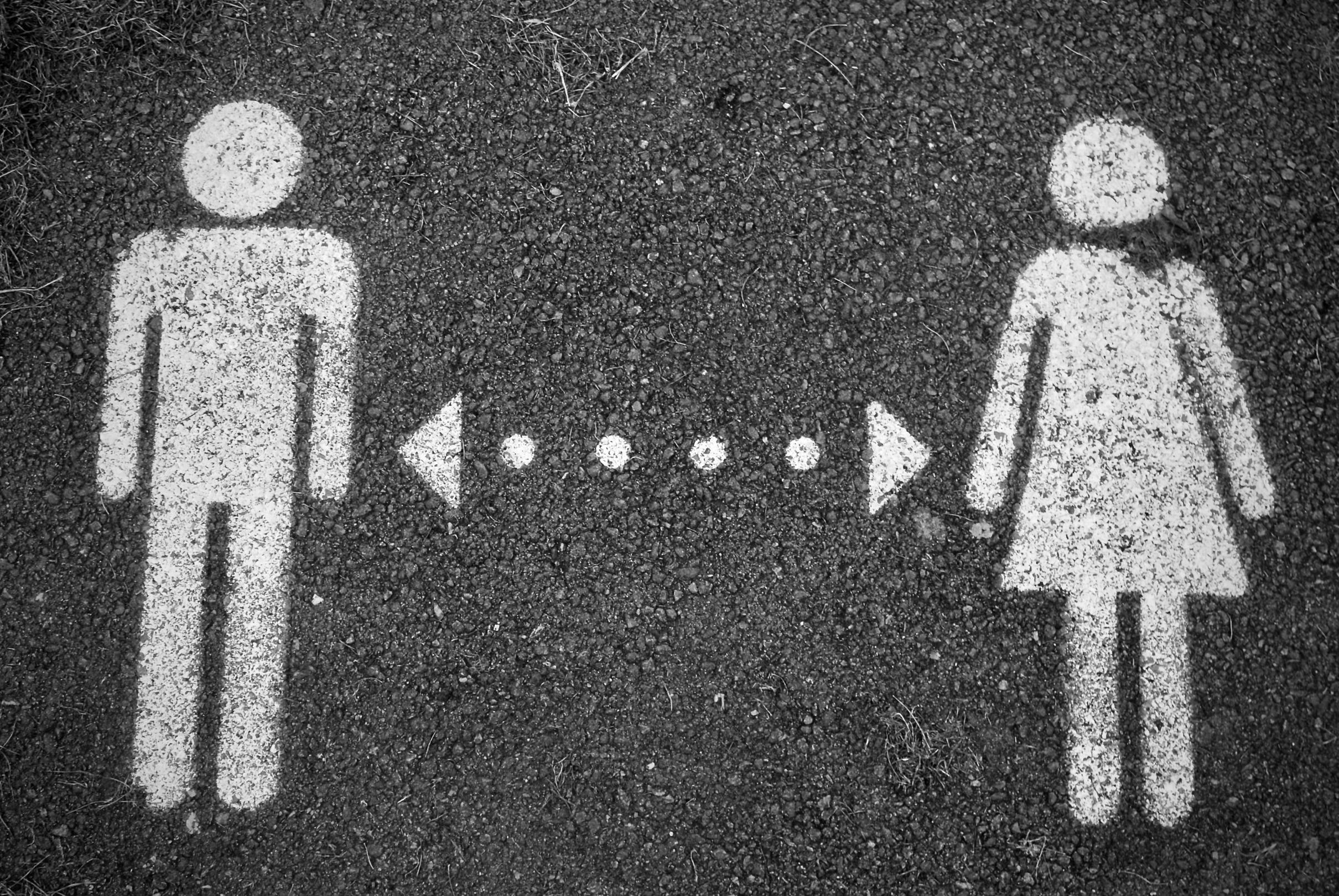 Symbol eines Mannes (links) und einer Frau (rechts), mit Kreide gemalt, dazwischen eine gepunktete Linie mit jeweils einem Pfeil nach rechts und links.