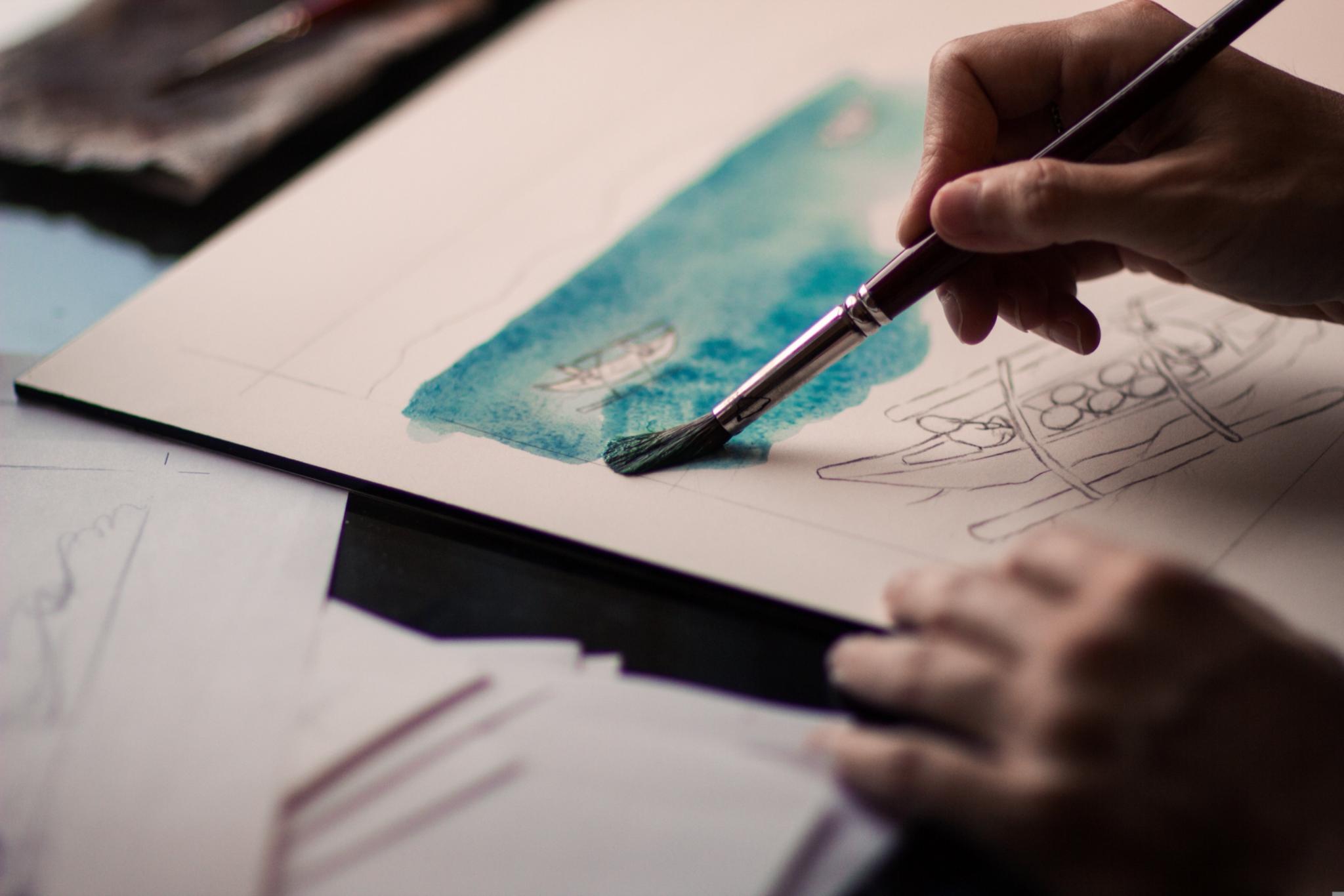 Hand einer Frau, die ein Aquarell malt.