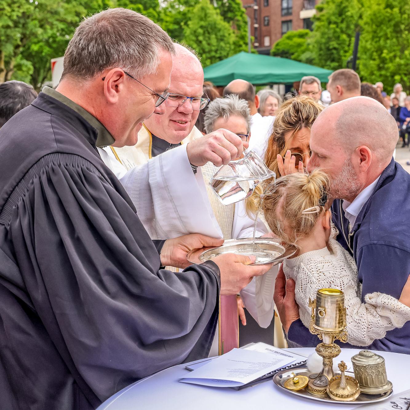 Während Regionalvikar Ulrich Clancett das Sakrament spendet, hält sein evangelischer Kollege Till Hüttenberger die Taufschale.