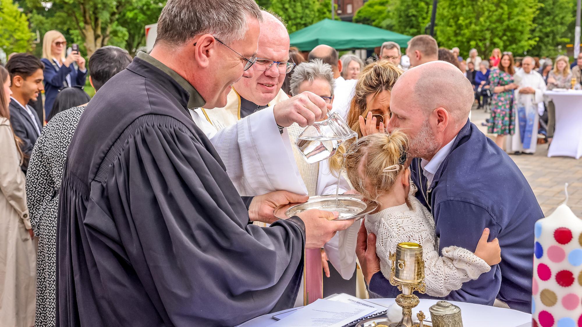 Während Regionalvikar Ulrich Clancett das Sakrament spendet, hält sein evangelischer Kollege Till Hüttenberger die Taufschale.