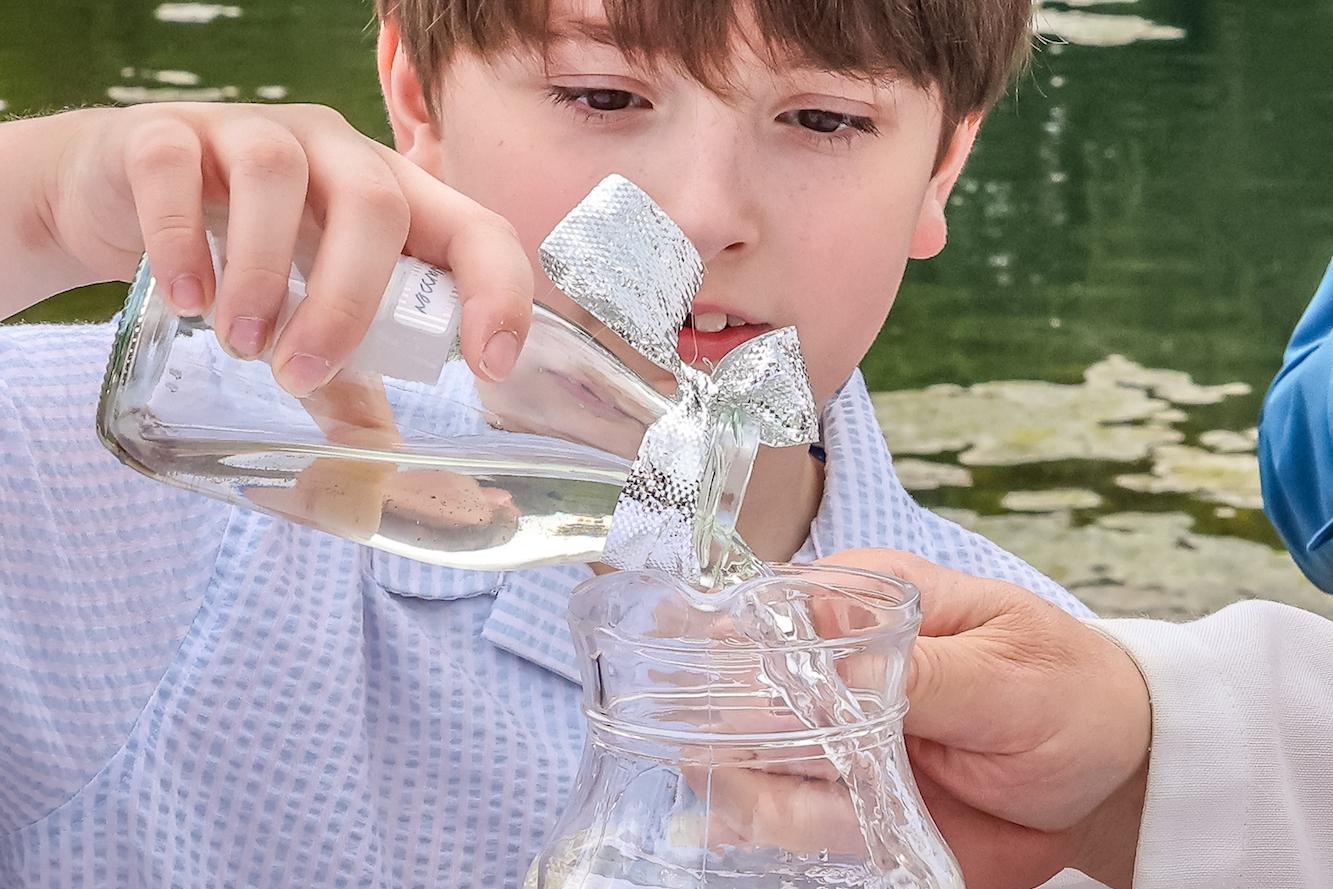 Ferdinand füllt das Wasser, das er morgens aus der Schwalm geschöpft hat, in den Krug. Damit wird der Achtjährige getauft.