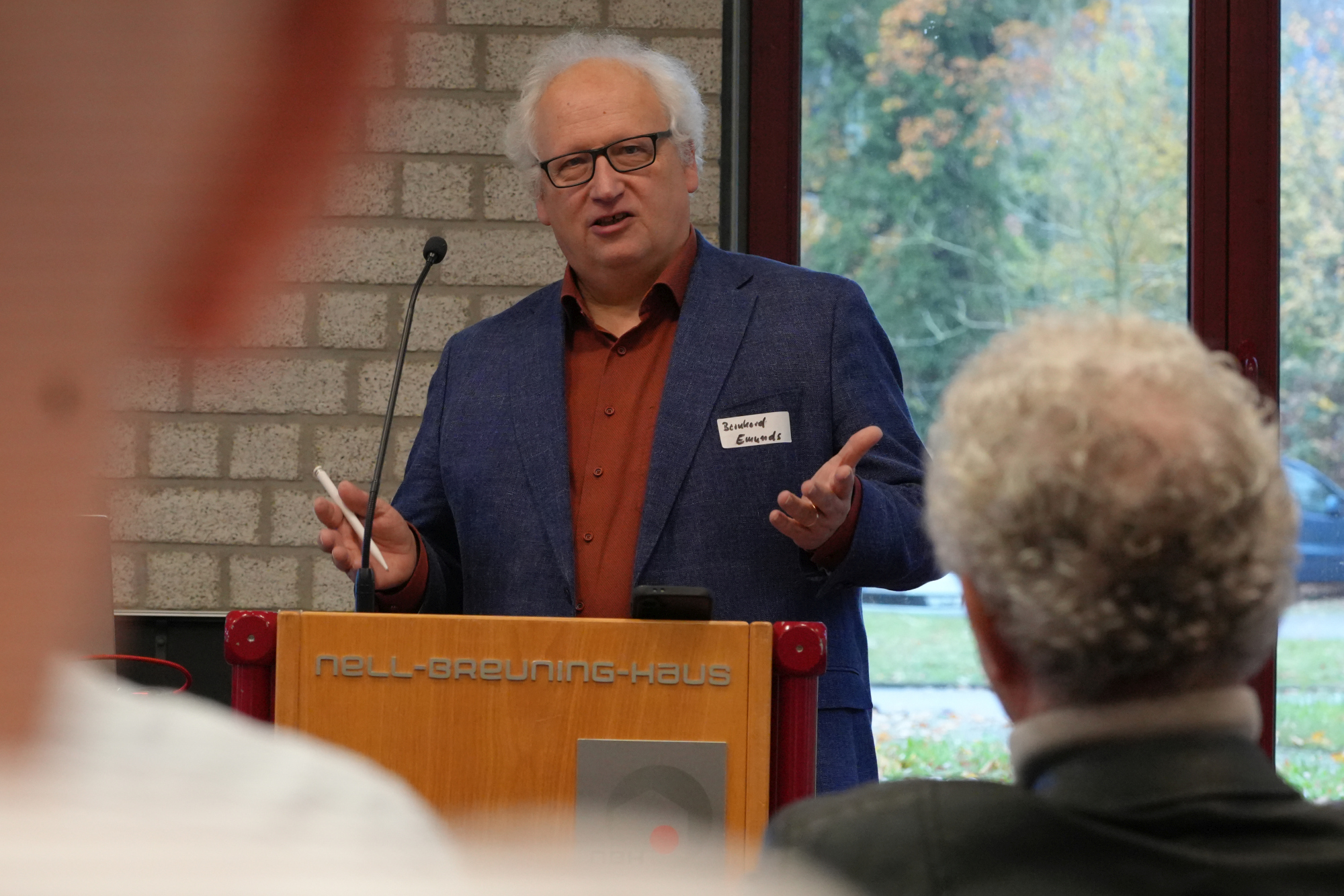 Ein Mann spricht am Rednerpult zu Menschen und hebt dabei die Hände.